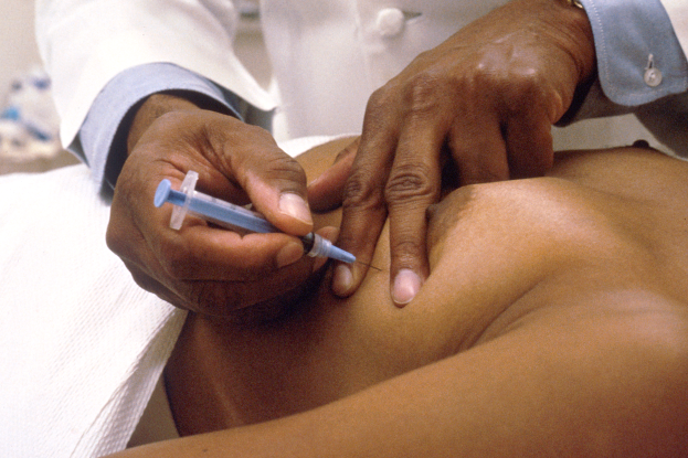 Ein Arzt in einem weißen Kittel verpasst einem Patienten auf einer weißen Unterlage eine Spritze.