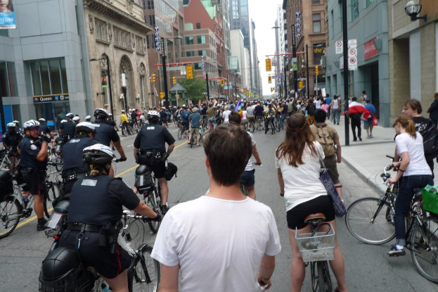 Gebäude säumen Straße, auf der einige Menschen Fahrrad fahren.