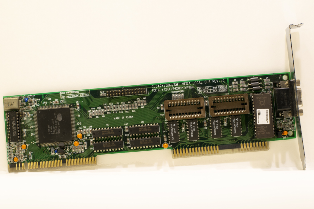 Nahaufnahme einer PCI-E-Karte auf einer weißen Oberfläche mit einem zentralen Chip und mehreren daran angeschlossenen Verbindern.
