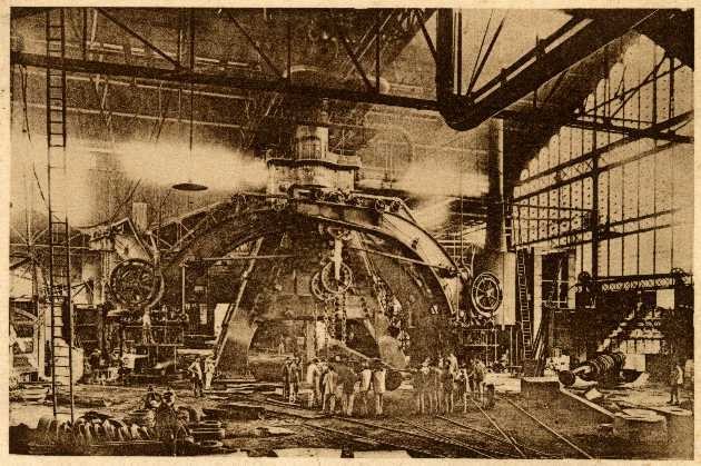 Schwarz-weiß-Foto eines Fabrikinneren mit Arbeitern, die eine große Maschine bedienen, umgeben von Leitern und Stangen, beschriftet mit "Cadillac Steel Works" unten.