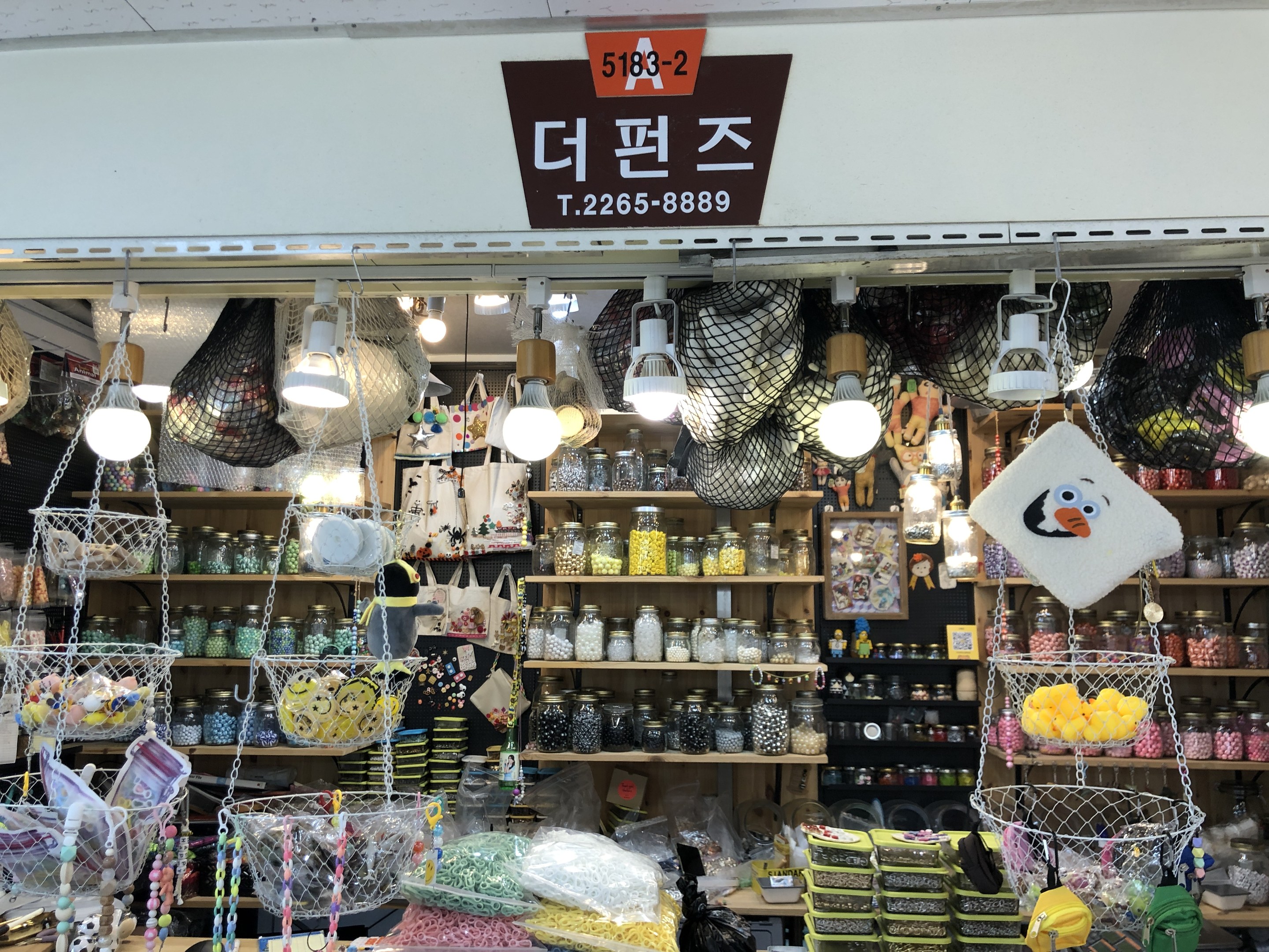 Ein unordentlicher Laden in Seoul mit verschiedenen Gegenständen wie Körben, Lampen, Flaschen und Spielzeugen auf Regalen, mit einer Tafel oben, die darauf hinweist, dass es einer der besten koreanischen Läden ist.