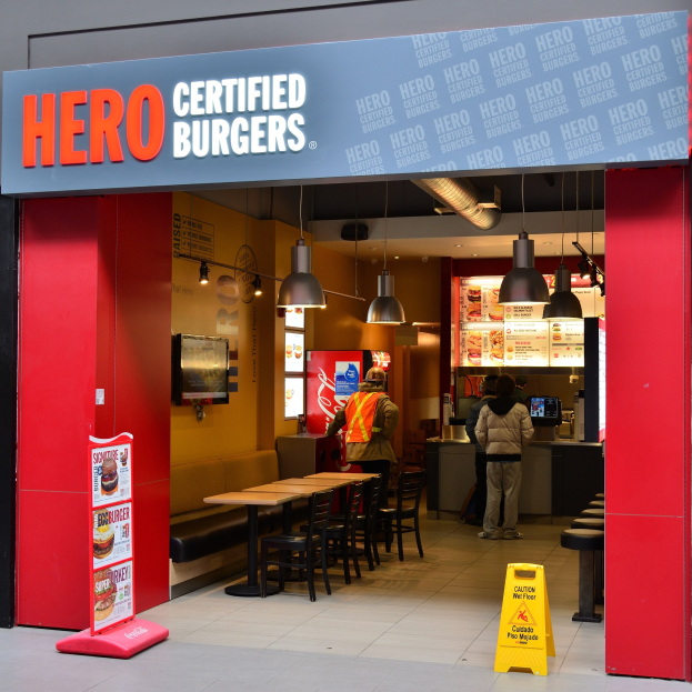 Außenansicht eines Hero Certified Burgers Restaurants in London, England, mit Gästen, Tischen, einer Speisekarte, einem Wandfernseher und Deckenleuchten.