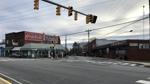 Stadtstraßenkreuzung mit Ampel, Fahrzeuge, Gebäude mit Schildern, Strommasten mit Drähten, Bäume und ein bewölkter Himmel.