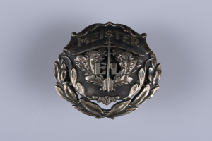 Ein silbern glänzender Abzeichenknopf mit einem Lorbeerkranz, dem Insigne der deutschen Armee, mit darauf eingravierter Inschrift, mittig auf einem einfarbigen Hintergrund.