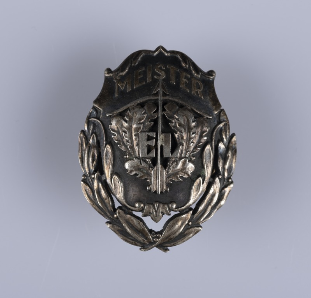 Ein silbern glänzender Abzeichenknopf mit einem Lorbeerkranz, dem Insigne der deutschen Armee, mit darauf eingravierter Inschrift, mittig auf einem einfarbigen Hintergrund.