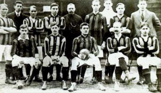 Schwarz-weiß-Foto einer Fußballmannschaft, einige stehen und einige sitzen, vor einer Wand mit dem Text "Ballymena Football Club" unten.