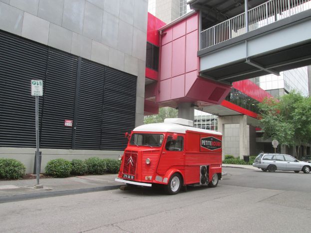 Ein Van steht in der Mitte des Bildes mit einem Auto auf der rechten Seite und Gebäude sind im Hintergrund sichtbar.