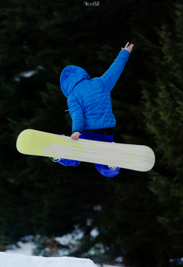 Ein Mann in einer blauen Jacke und Hose führt Eiskunstlauf-Stunts auf dem Schnee mit Bäumen im Hintergrund aus.