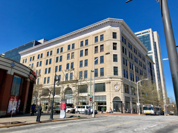 Großes Gebäude als Washington Post Office identifiziert mit vielen Fenstern, umgeben von Straßenmasten, Straßenlaternen, Kraftfahrzeugen, Fußgängern, Informationsschildern und Bäumen unter einem bewölkten Himmel.