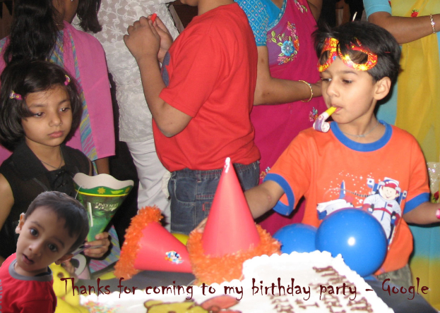 Kinder stehen vor einem Tisch mit einem Kuchen, Luftballons und Mützen, mit anderen Personen im Hintergrund.