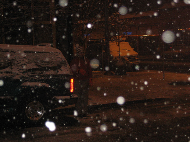 Eine dunkle Szene mit Schneefall und zwei Fahrzeugen auf einer Straße.