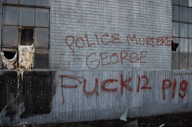 Graffiti an einer Gebäudewand mit der Aufschrift "Polizei Mord George Fuck 12 P19" und Fenstern sowie verstreuten Gegenständen davor.