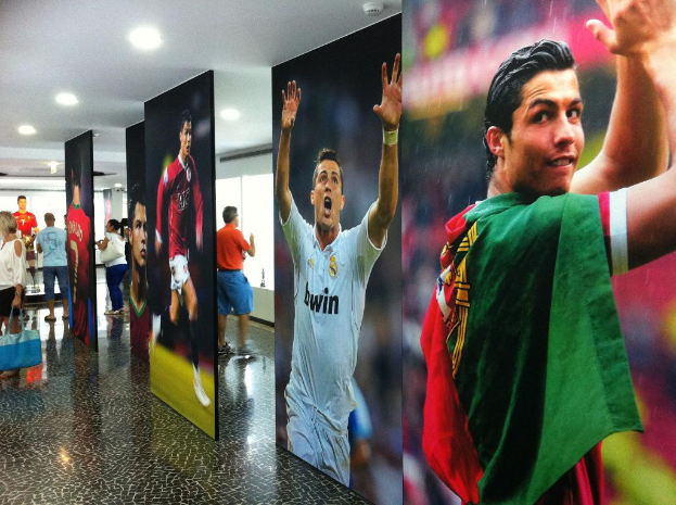 Ein Banner mit dem Fußballspieler Rolando, mit Menschen, die links neben einem Tisch stehen, und Lichtern oben.