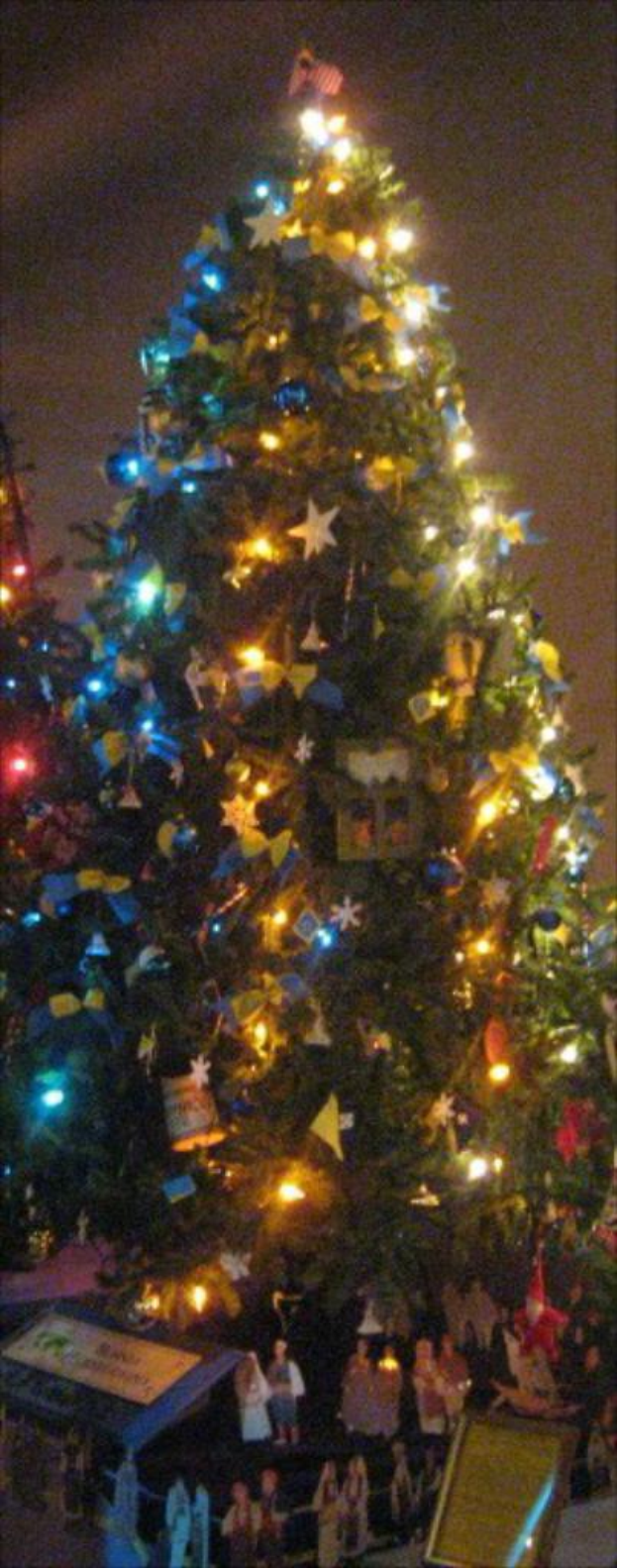 Ein geschmückter Weihnachtsbaum mit darunter auf einem Tisch platzierten Menschenstatuen.