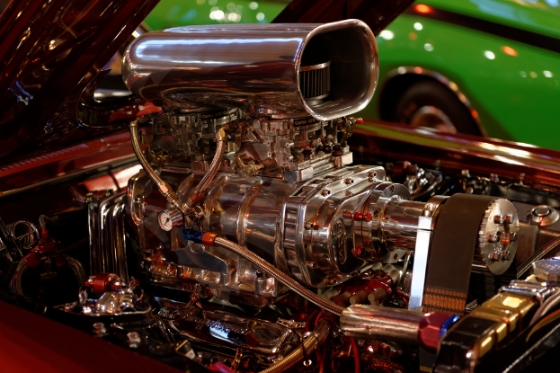 Eine Sammlung von Fahrzeugmotorteilen und anderen Komponenten mit einem im Hintergrund sichtbaren Auto.