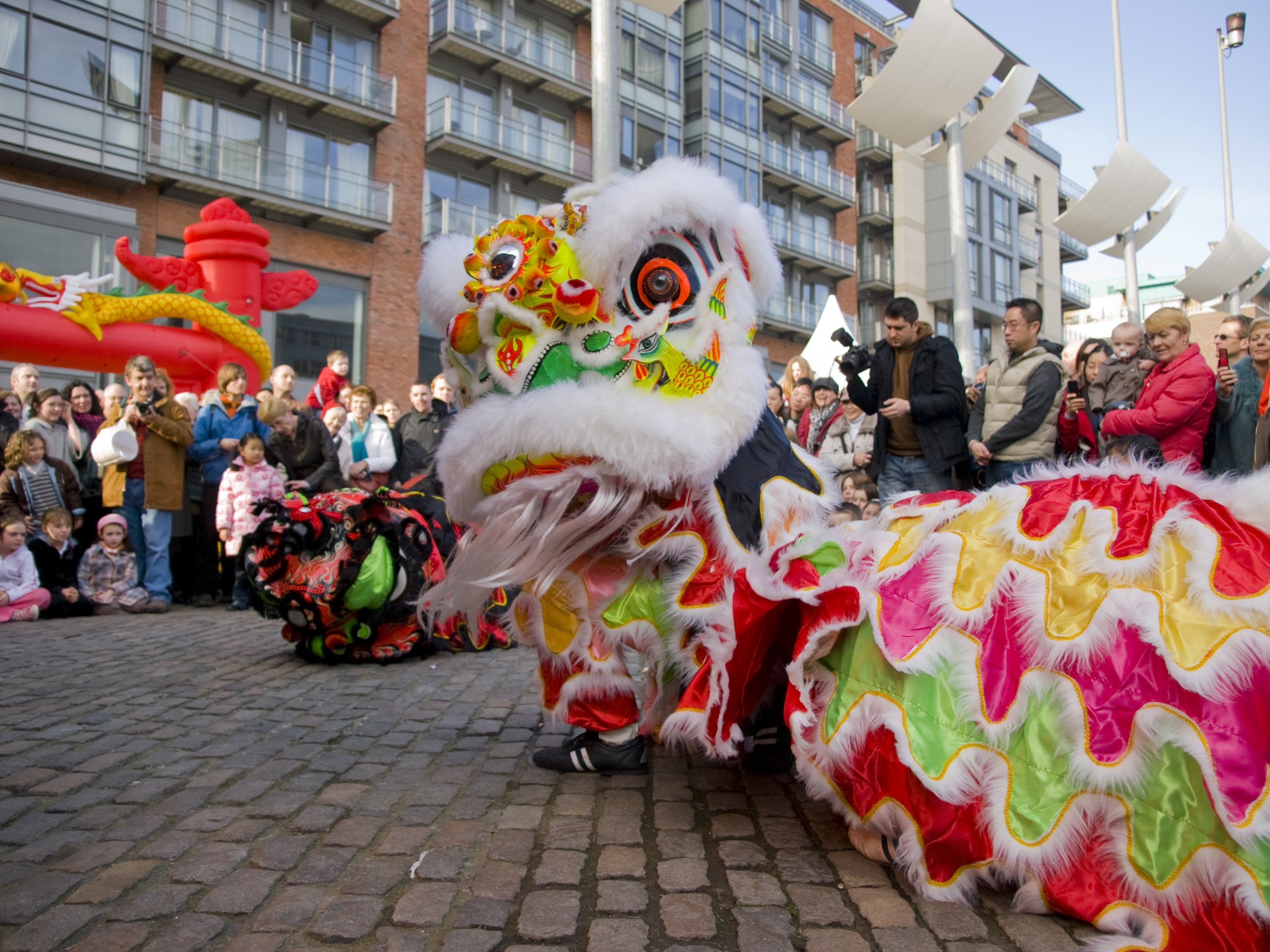 Vibrantes chinesisches Neujahrsfest in Amsterdam mit Löwen tanzen vor Menschenmenge und Gebäuden unter klarem Himmel.