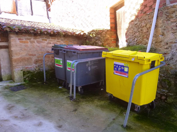 Zwei gelbe und graue Mülltonnen mit Rädern nebeneinander vor einem Gebäude mit einer Wand und einem Fenster.