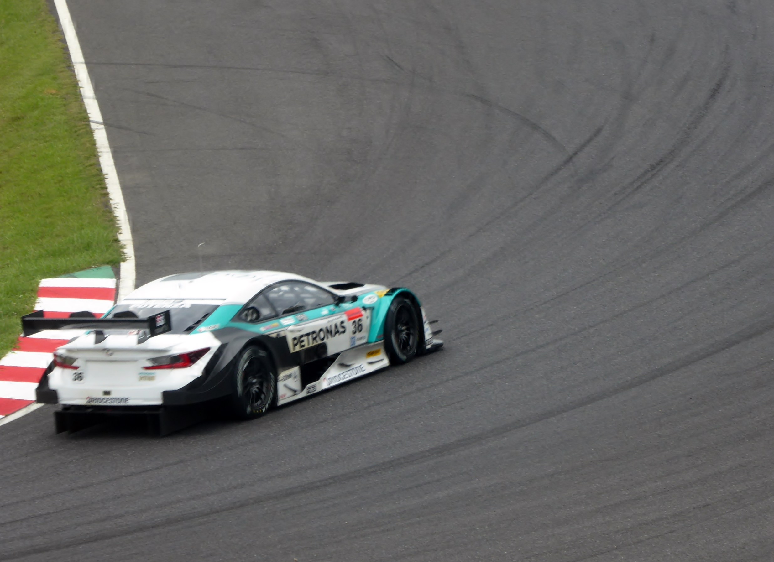 Ein Mercedes-AMG GT3 Rennwagen auf einer Rennstrecke mit Text auf der Karosserie und Gras links.