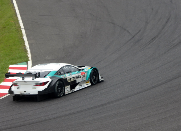 Ein Mercedes-AMG GT3 Rennwagen auf einer Rennstrecke mit Text auf der Karosserie und Gras links.