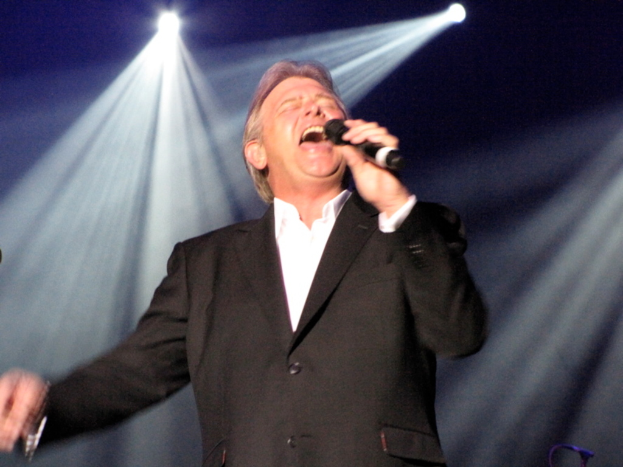 Ein Mann mit Mikrofon auf der Bühne singend mit Lichtern im Hintergrund.