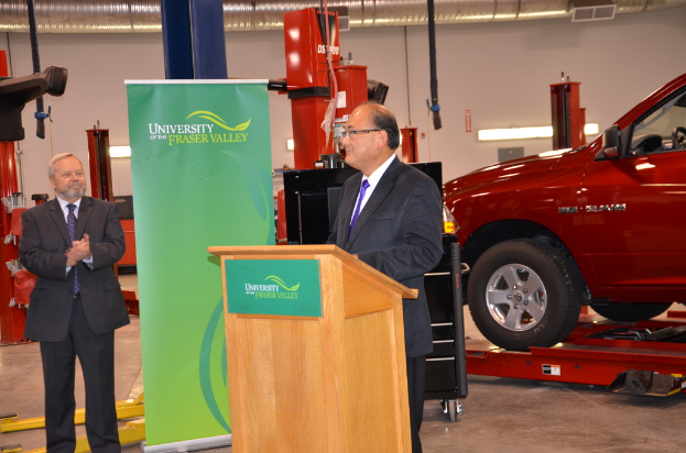Zwei Männer in Anzügen auf dem Boden mit einem roten Fahrzeug, Banner, Podium und diverser Ausrüstung im Hintergrund.