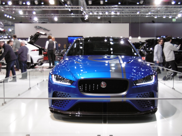 Ein blauer Jaguar XE SV Project 8 wird auf der Frankfurter Motor Show präsentiert, umgeben von Menschen und beleuchtet von Deckenlampen, mit einem Fernseher im Hintergrund.