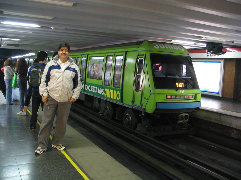 Ein Zug auf Eisenbahnschienen mit Menschen, die links stehen und ein Dach an der Spitze des Bildes.