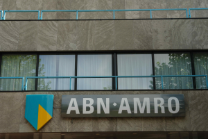 Ein Gebäude mit einer Tafel, auf der "ABN AMRO" steht, mit einer Tafel mit Text, Geländern und Glasfenstern mit Vorhängen, mit Text unten, der eine Strafe von 1,5 Milliarden Dollar durch die Europäische Union erwähnt.