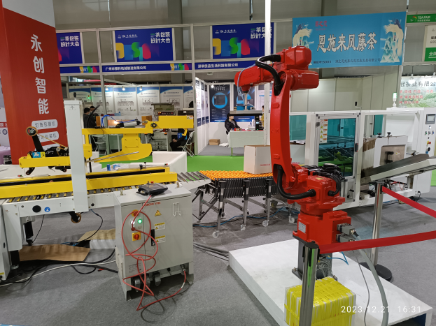 Eine Gruppe von Robotern auf einem Tisch umgeben von Maschinen und Kabeln in einer Fabrikumgebung mit ein paar Menschen im Hintergrund.