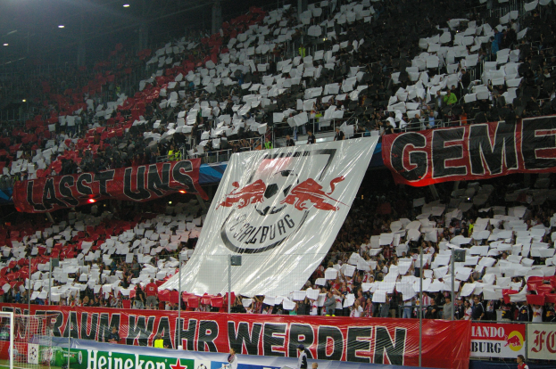 Ein volles Fußballstadion mit Sitz- und Stehplätzen, Banner, einem Torpfosten und Überdachungsbeleuchtung.