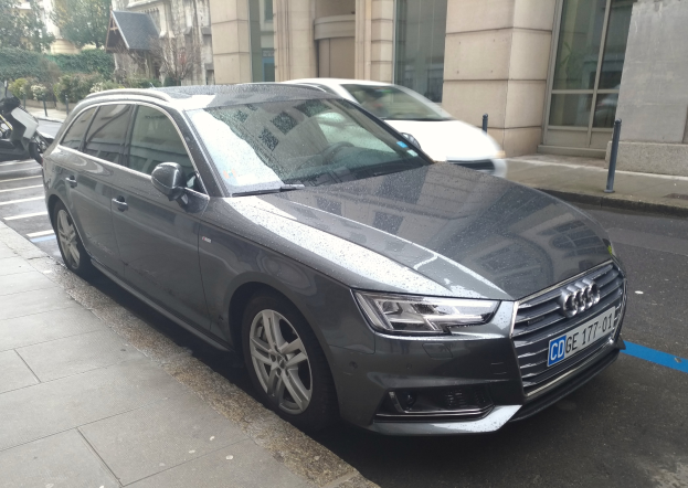 Ein Audi A4 Avant 2.0 TDI Quattro Tiptronic S Tronic S Line auf einer Straße mit Gebäuden, Bäumen, Pflanzen und Polen unter einem klaren blauen Himmel.