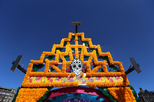 Ein Día de los Muertos-Bogen, der mit Blumen und einem Schädel geschmückt ist, steht in Mexiko-Stadt und ist von Gebäuden unter einem klaren blauen Himmel umgeben.