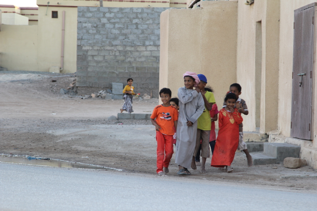 Eine Gruppe lachender Kinder, die gemeinsam im Freien stehen, mit Gebäuden, Wasser, Felsen und einer Straße im Hintergrund.