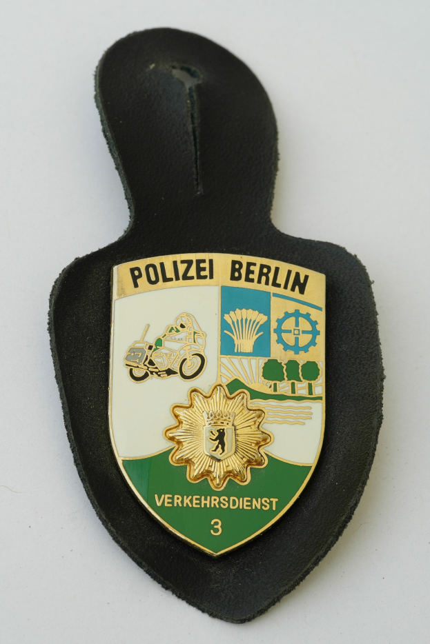Polizei Berlin Abzeichen mit einem blauen Schild, weißer Grenze, zentralem weißen Stern und schwarzer fetter Schrift auf einer Oberfläche.