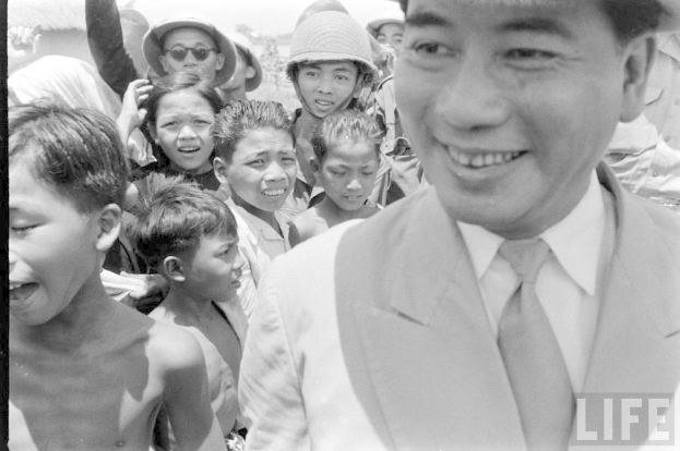 Ein Schwarz-Weiß-Bild von Kindern mit einer Person auf der rechten Seite, die Kleidung trägt und einen Text in der unteren rechten Ecke.