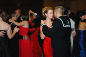 Eine Gruppe von Menschen in Abendgarderobe tanzt energisch auf einer Tanzfläche mit einer Wand im Hintergrund.