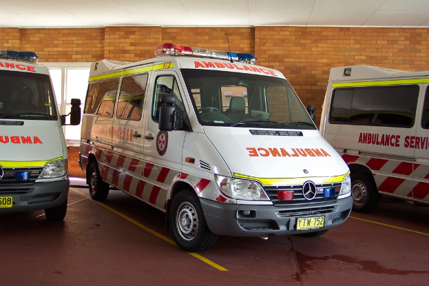 Ein weißer Krankenwagen steht vor einer Backsteinmauer.