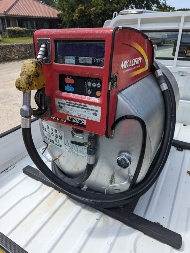 Ein Lastwagen mit einer Gasträgerpumpe auf der Ladefläche parkt neben einem Haus, umgeben von Bäumen unter einem klaren blauen Himmel.