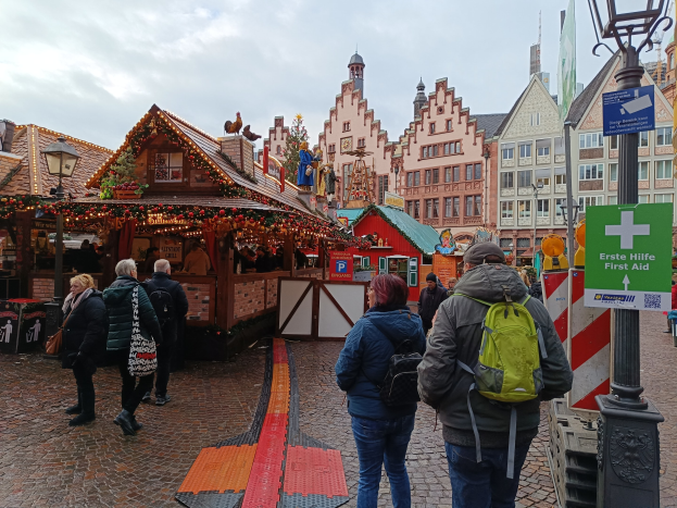 Menschen, die auf einem Kopfsteinpflasterweg neben einem Weihnachtsmarkt in Nürnberg, Deutschland, gehen, mit Laternenmasten und Informationsschildern im Blickfeld.