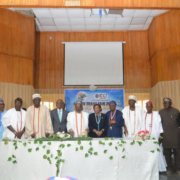 Gruppe von Menschen um einen weißgedeckten Tisch versammelt auf der ICCI International Trade Fair 2019, mit einem Banner, Projektionsbildschirm und Deckenbeleuchtung im Hintergrund.