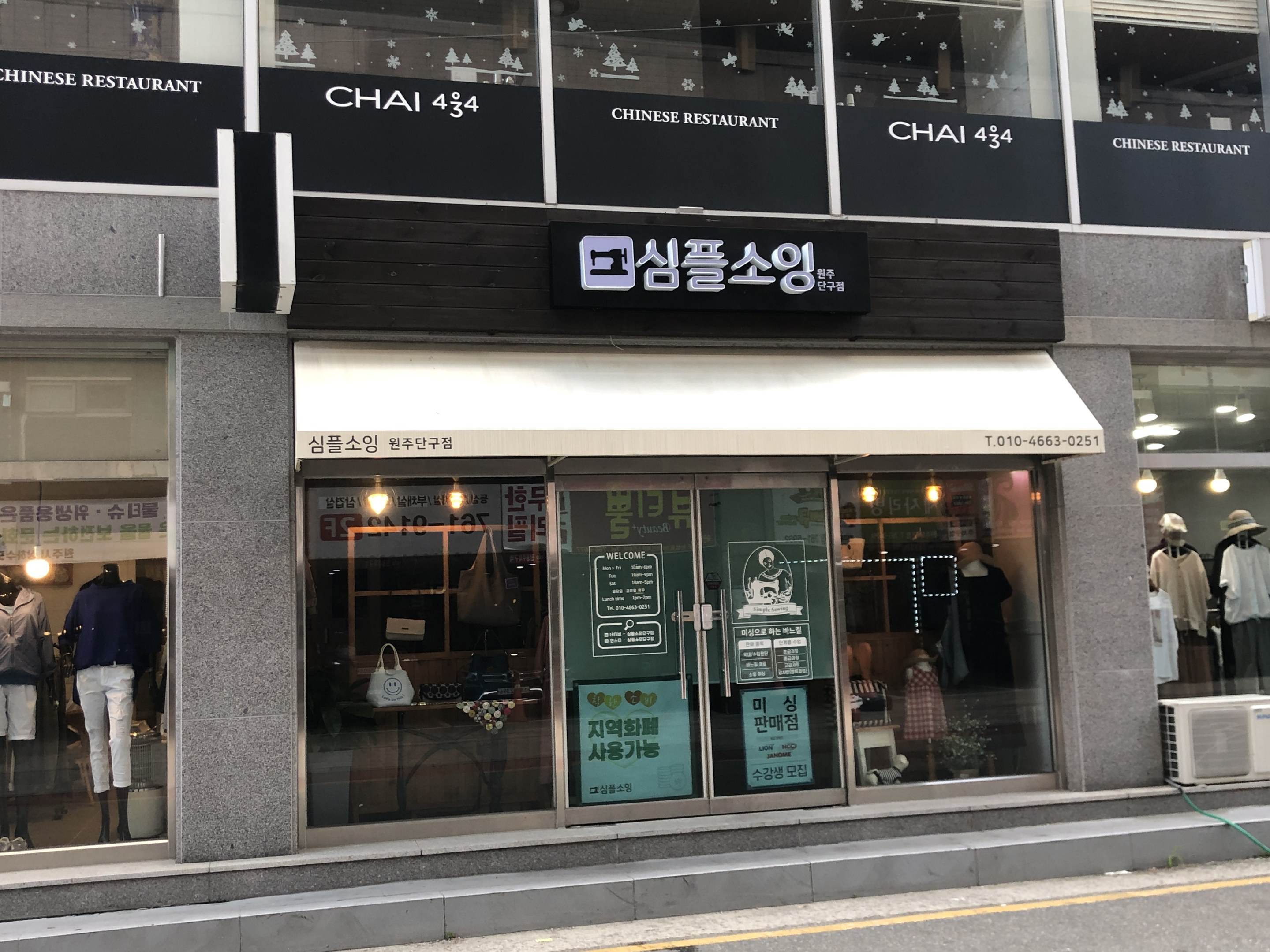 Außenansicht des Chai 434 Chinesischen Restaurants in Seoul, Südkorea, mit Glaswänden, Schaufensterpuppen in Kleidern, beleuchteten Schildern, einer Klimaanlage auf der rechten Seite und einer Straße unten.