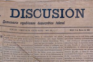 Eine gelbliche, leicht zerknitterte Zeitung mit der Überschrift "Semanario Repúblicano Democrático Federal" und dem Wort "Diskussion" in schwarzer Tinte geschrieben.