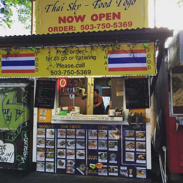 Ein Geschäft mit verschiedenen Artikeln, darunter Getränkedosen, Speisekarten, eine Uhr, Gewürze in Plastikbehältern, Gewürze, Werbetafeln, Namensschilder und ein Blick auf den Himmel.