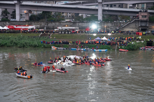 Eine Gruppe von Menschen in kleinen Booten auf einem Gewässer, umgeben von Vegetation und Gebäuden, mit Schwimmwesten bei einer Rettungsaktion.