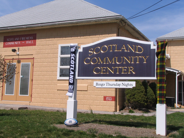Außenansicht des Scotland Community Center mit einem Schild, Gras, einem Ball, Pflanzen, einem Baum, sichtbaren Drähten und einem bewölkten Himmel.