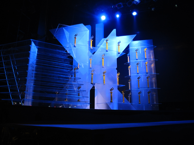 Eine Bühne für eine Preisverleihung mit dunklem Hintergrund, beleuchtet von ein paar Lichtern und mehreren Gegenständen, die mit dem Event in Verbindung stehen.