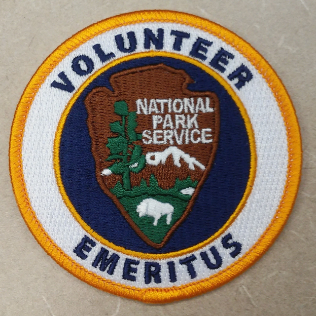 Runder Flicken mit blauem Rand und weißem Hintergrund, der den schwarzen Text "Volunteer National Park Service Emeritus" in der Mitte eines gelben Kreises zeigt.