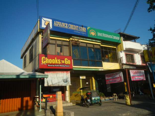 Ein Gebäude mit einer Tafel, auf der "Advance Credit Corp" steht, an einer Straße mit Fahrzeugen, Werbetafeln, Strommasten und Bäumen unter einem klaren blauen Himmel.