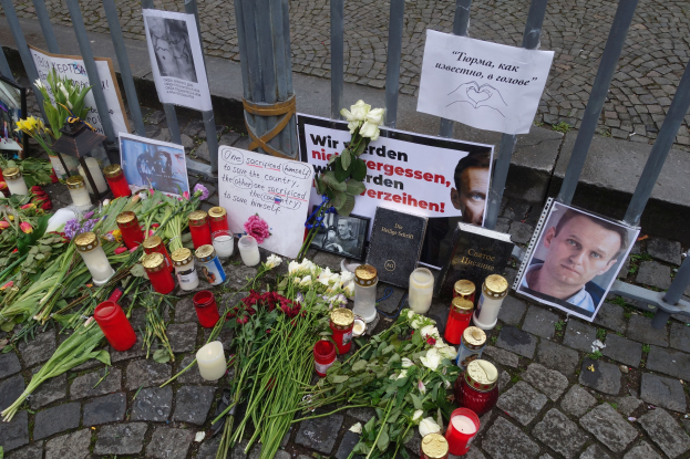 Mahnmal in Berlin, Deutschland, mit Huldigungen wie Blumen, Kerzen, Fotos und Plakaten, die auf dem Boden vor einem Zaun aufgestellt sind.