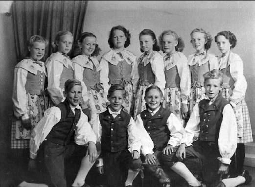 Ein Schwarz-Weiß-Foto einer Gruppe von Kindern, die vor einer Wand mit einem Vorhang posieren, mit dem Text "1930er Kinder-Schule" unten.